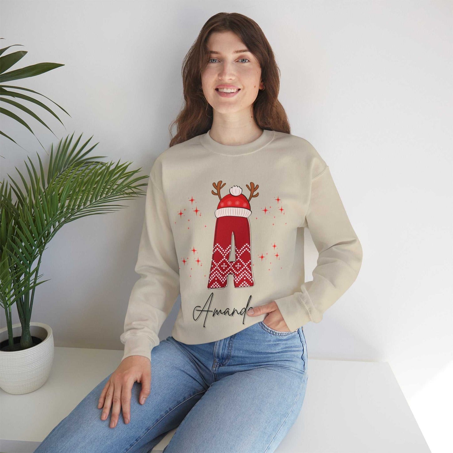 Family Christmas Name Sweatshirt with personalized design featuring a festive reindeer hat, modeled by a woman sitting on a table, perfect for holiday celebrations.