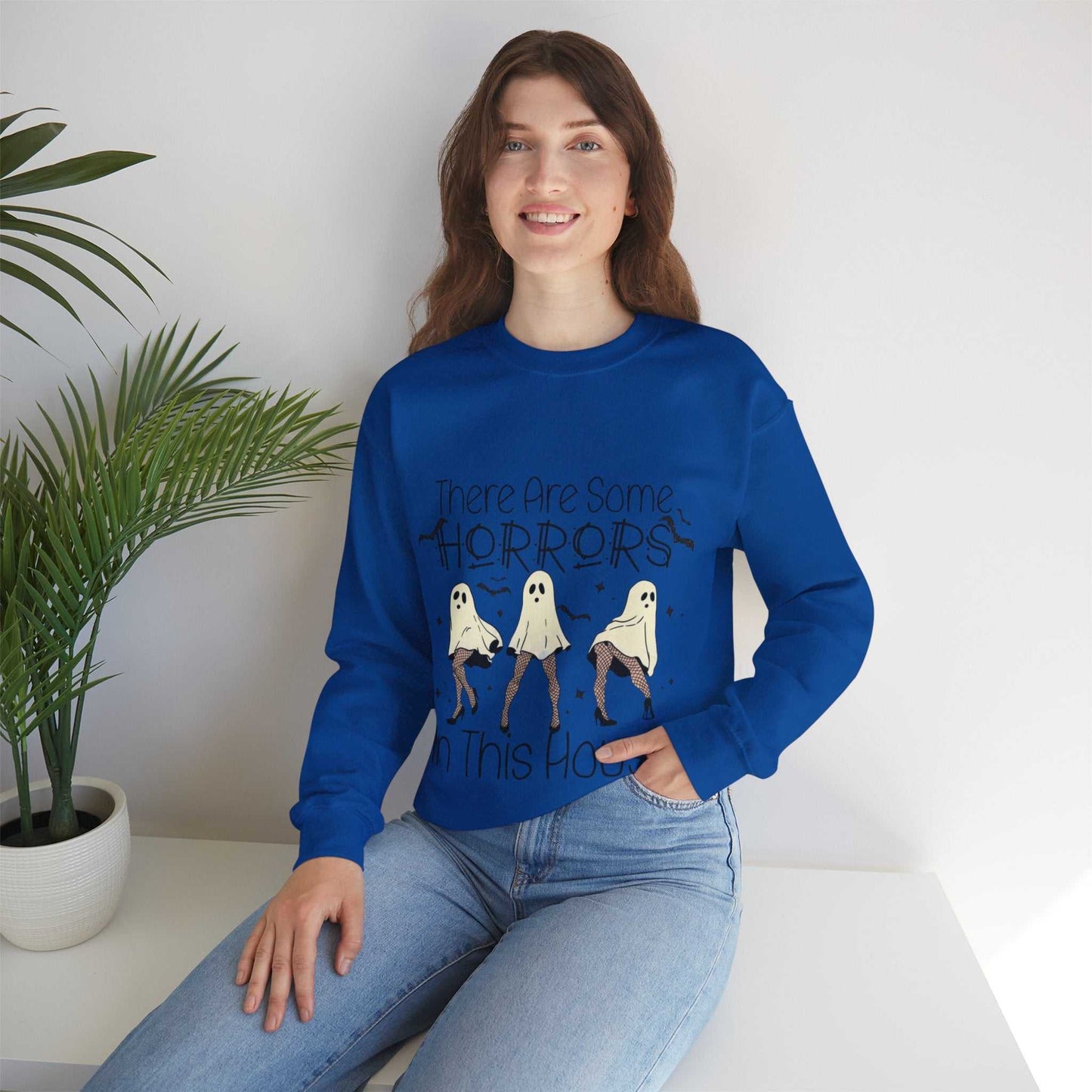 Funny Halloween Sweatshirt with ghost design and text "There Are Some Horrors in This House", worn by woman sitting inside.