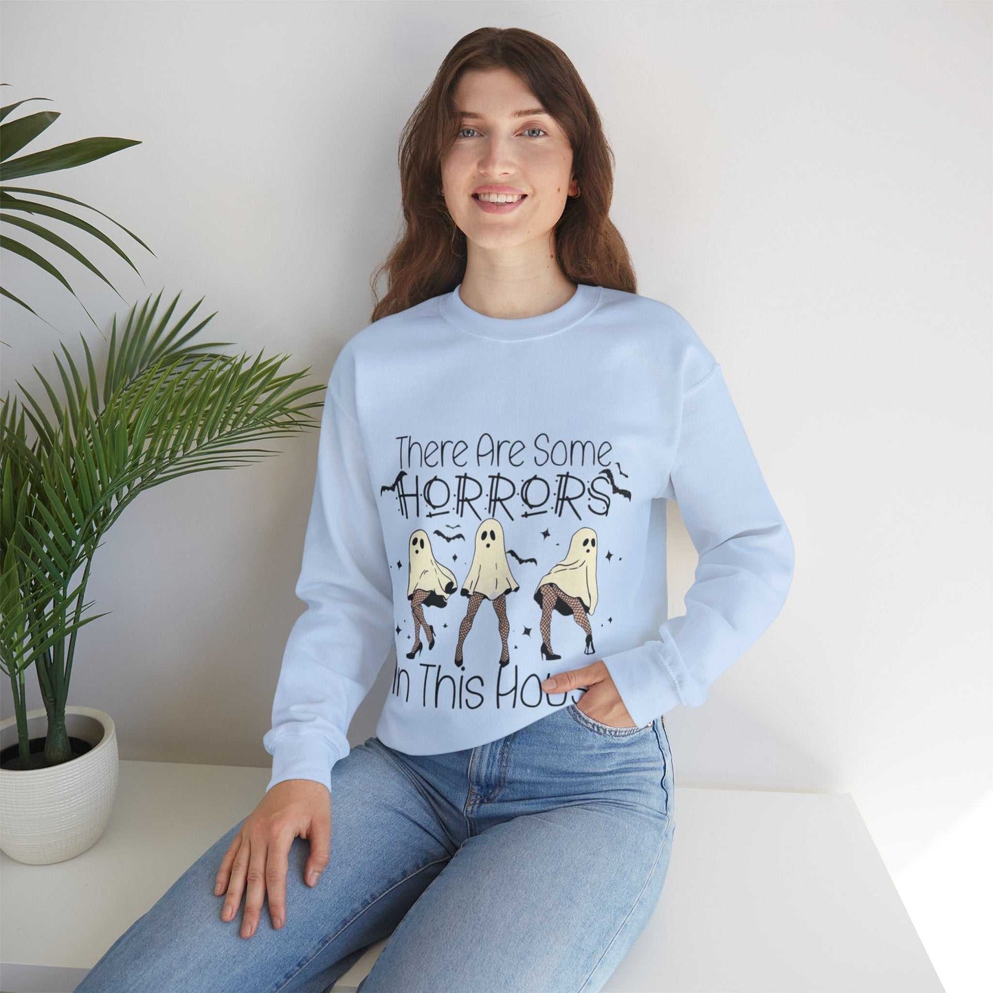 Woman wearing a Funny Halloween Sweatshirt with "There's Some Horrors in This House" design, featuring comfortable unisex style in polyester and cotton blend.