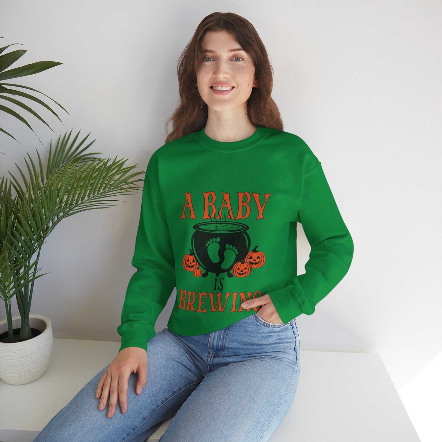 Unisex green sweatshirt with "A Baby Is Brewing" text and Halloween design, perfect for pregnancy announcements.