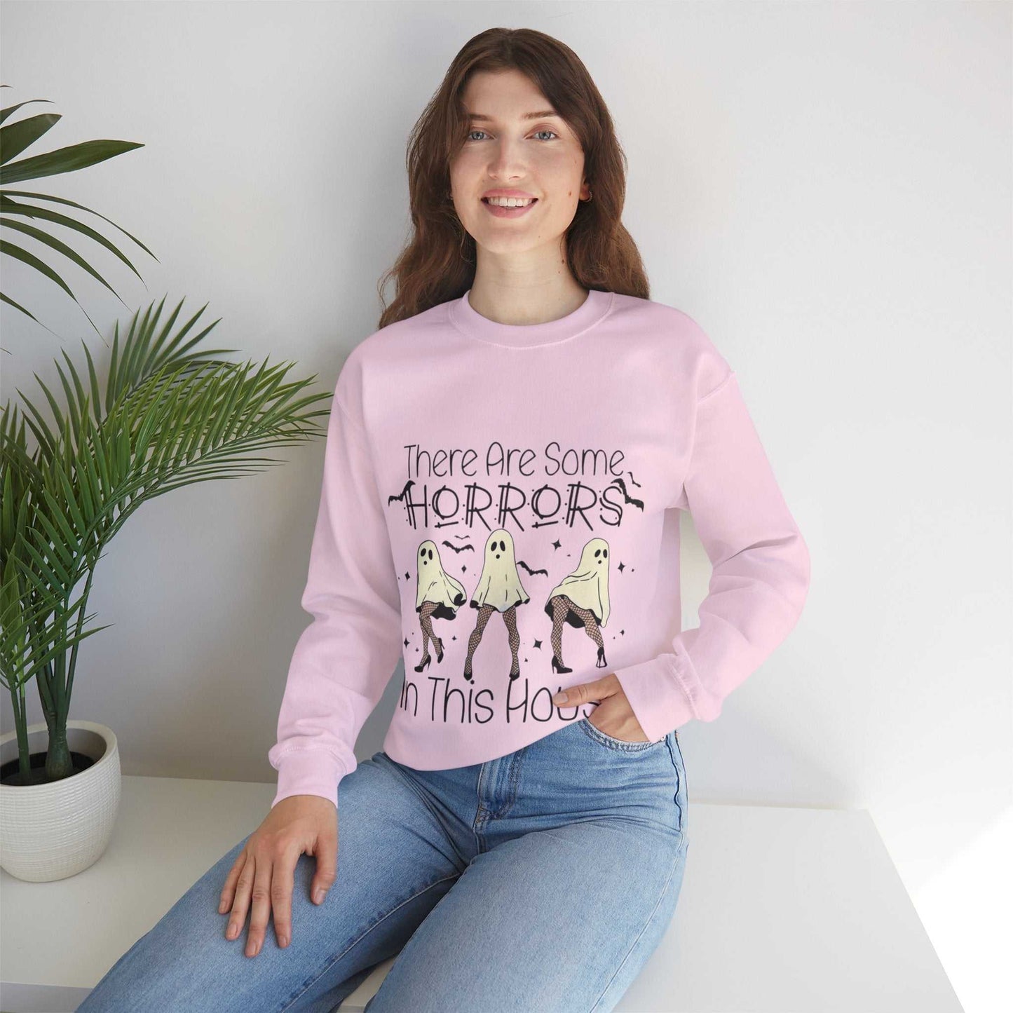 Funny Halloween sweatshirt with "There's Some Horrors in This House" design, featuring a unisex heavy blend crewneck in pink.