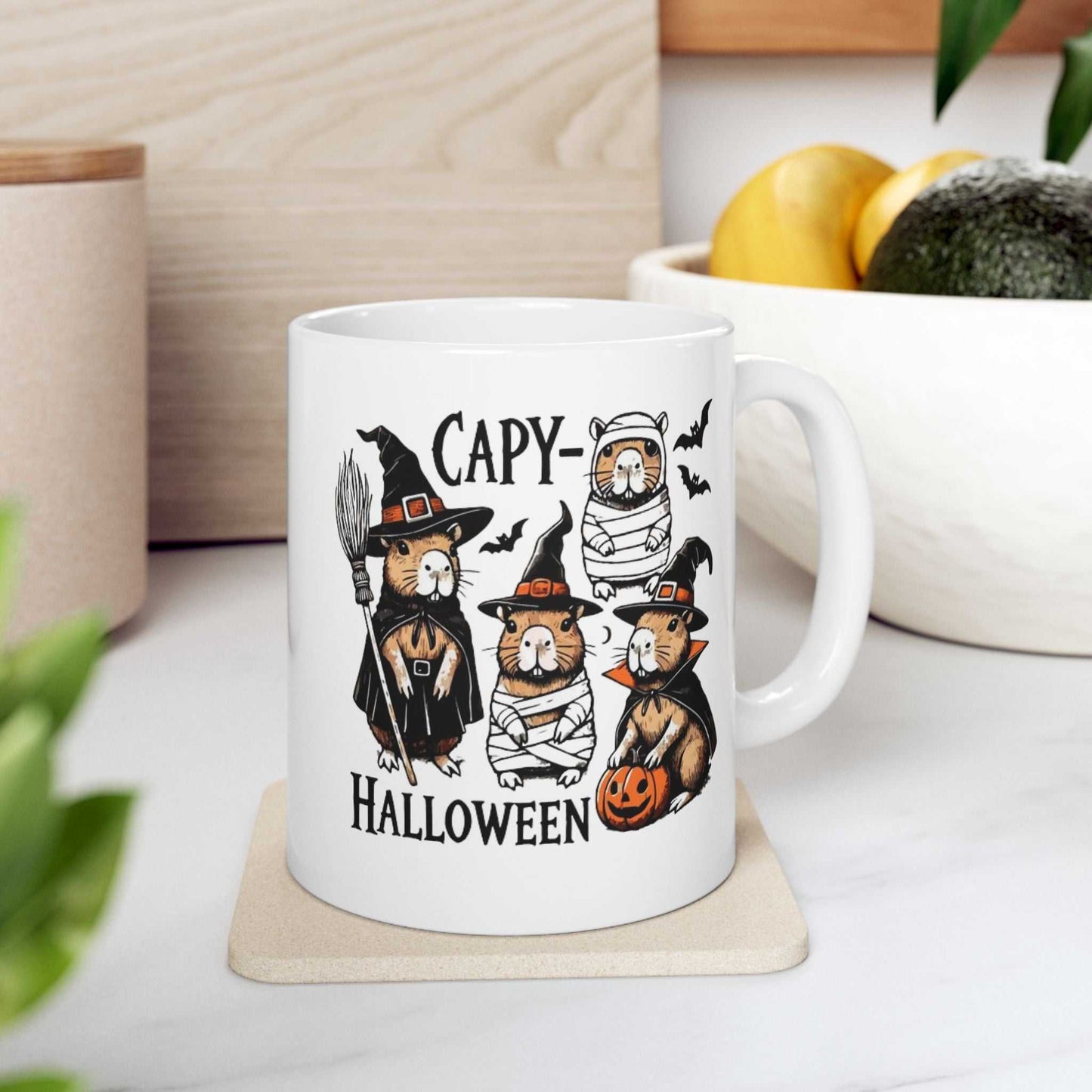 Halloween-themed ceramic coffee mug featuring capybaras in spooky costumes with pumpkins and bats.