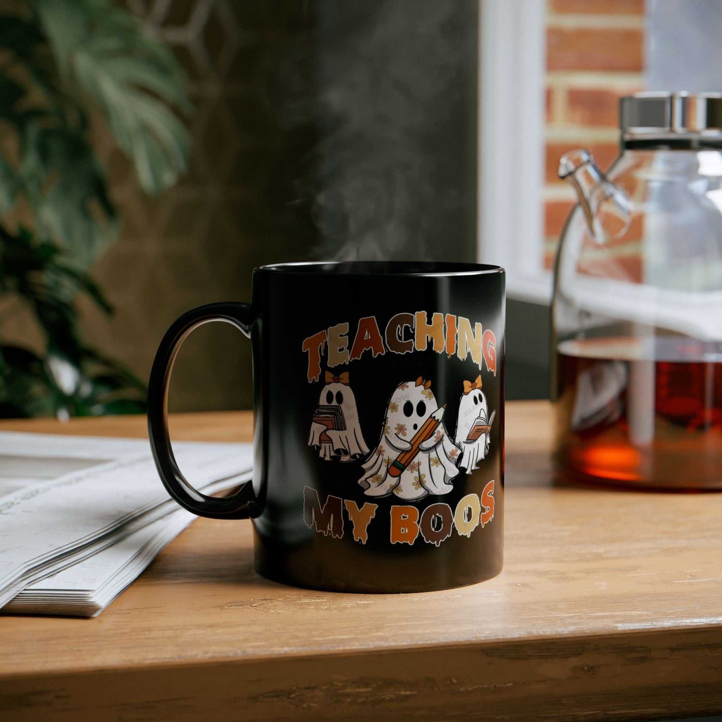 Black ceramic Halloween mug with ghost designs and "Teaching My Boos" text, perfect for teachers, available in 11 oz and 15 oz sizes.