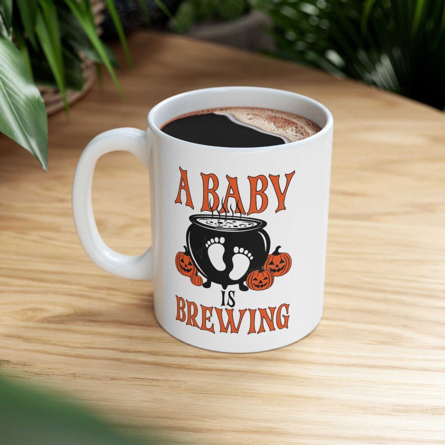 White ceramic mug with "A Baby is Brewing" Halloween-themed design, featuring vivid colors; perfect for pregnancy announcements.
