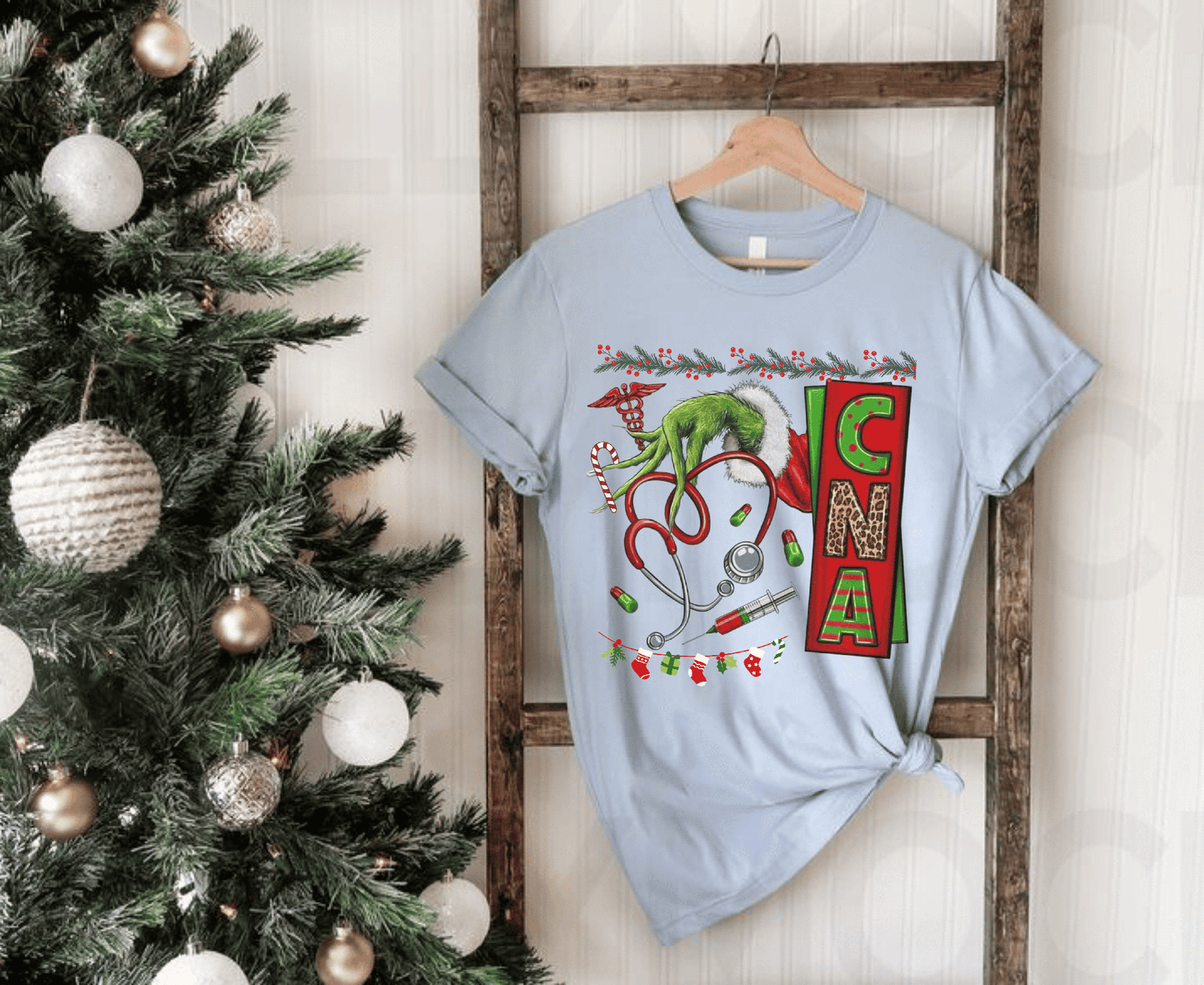 Nurse stethoscope Christmas T-shirt with Grinch design hanging by holiday tree.